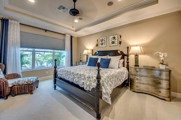 Master bedroom king bed with tray ceiling, palm view window, and wicker accent chair