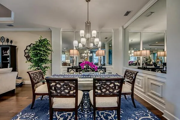 Formal dining room with dark wood table, blue patterned rug, mirror panels, chandelier