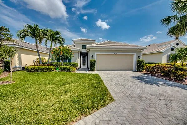 Front elevation of the home with paver driveway and manicured tropical lawn
