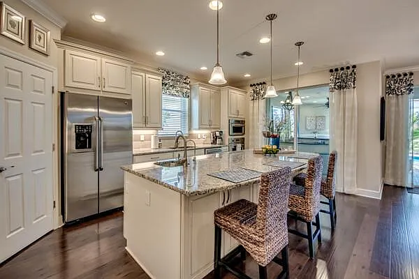 Kitchen island with wicker barstools, stainless fridge, pendant lights