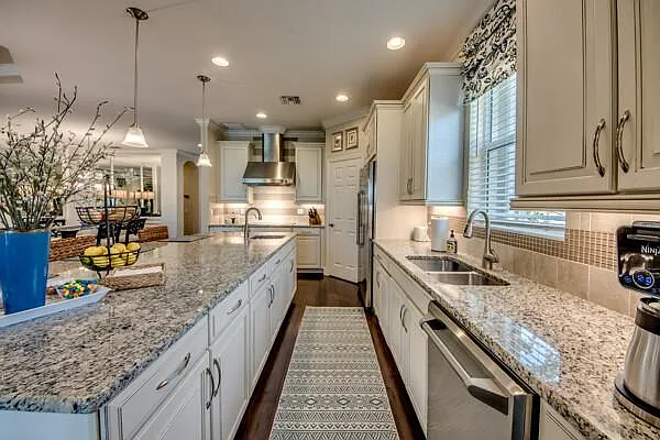Kitchen with white cabinets, granite island, pendant lights, and view to dining room