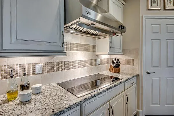 Kitchen cooktop with designer range hood, mosaic tile backsplash, gray/white cabinets