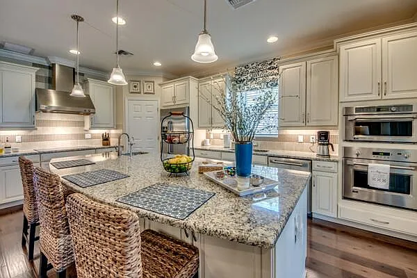 Kitchen with white cabinets, large granite island, double wall ovens, and barstools