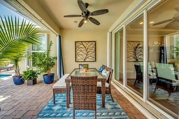 Covered lanai dining set with wicker chairs, lush plants, and sliding glass door