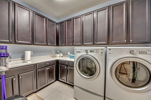 Laundry room with front-load washer and dryer, dark cabinets, countertop and sink
