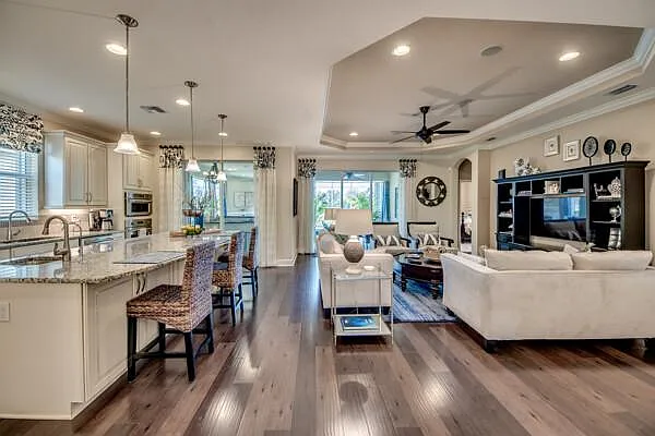 Wide view of open-plan living room and kitchen with beige sectional and tray ceiling