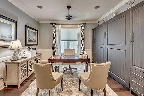 Home office with dark wood desk, two upholstered chairs, and Murphy bed cabinet